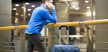 Mann mit Koffer steht am Flughafen und telefoniert